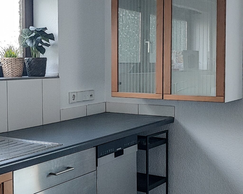 Küche der Ferienwohnung mit Hängeschrank mit Glastüren und Pflanzen auf der Fensterbank