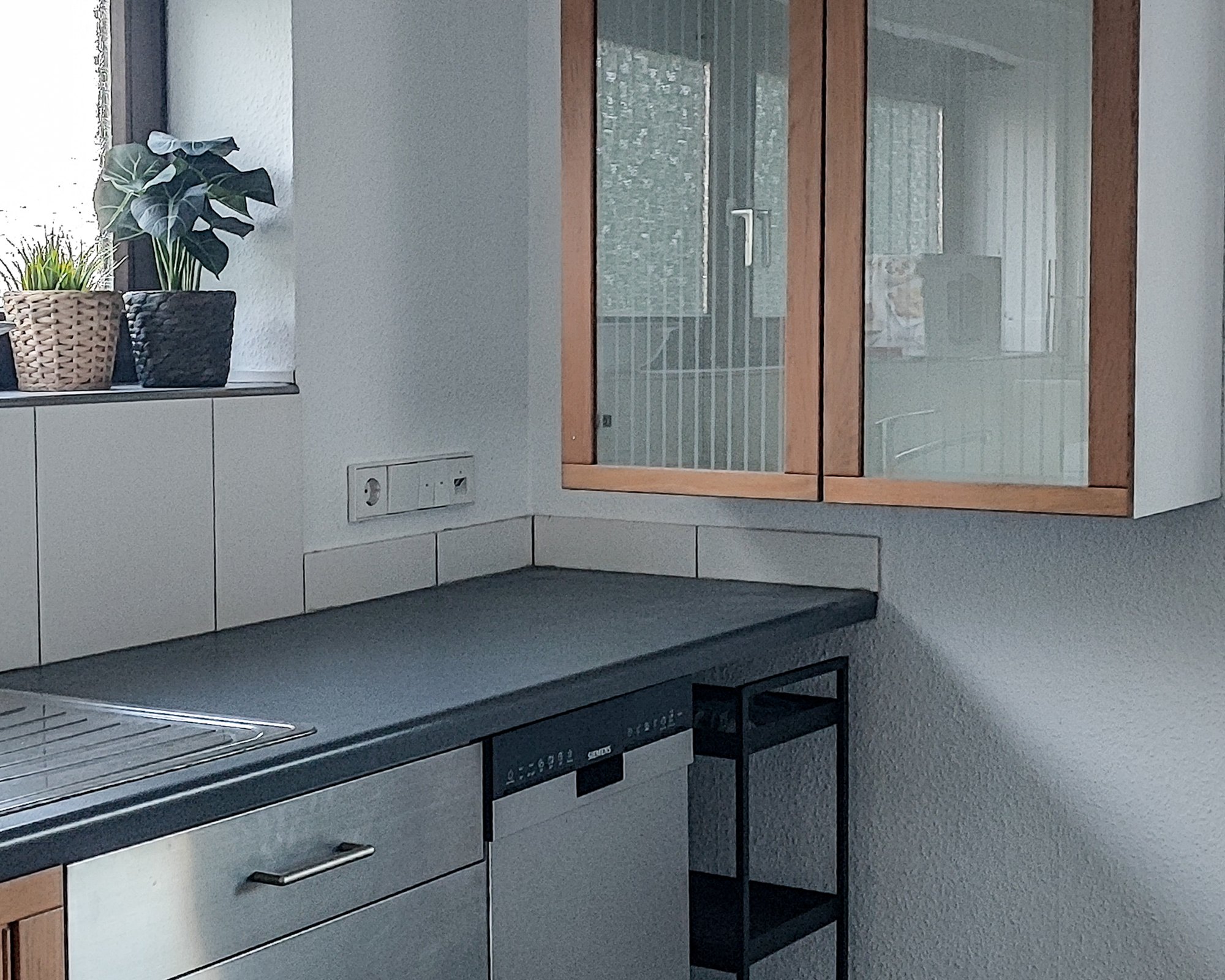 Küche der Ferienwohnung mit Hängeschrank mit Glastüren und Pflanzen auf der Fensterbank