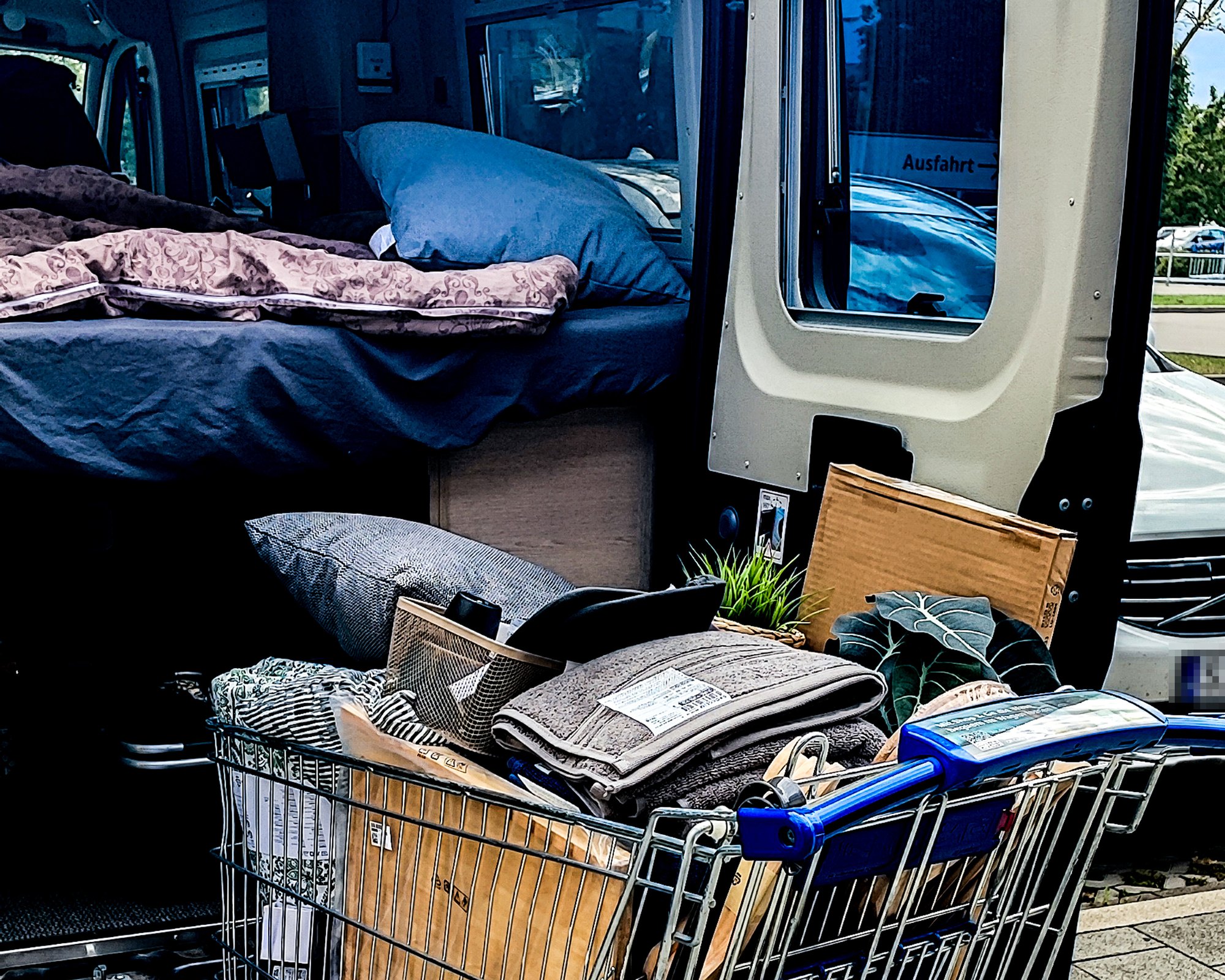 Camper mit Bett und Einkaufswagen voller Textilien, Kissen und Pflanzen
